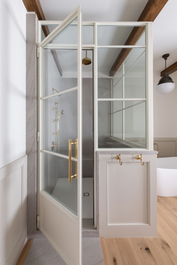 A white steel shower unit. EURO-LITE Casement with golden hendles, white walls, and wood floors. Cozy modern glass and steel design.